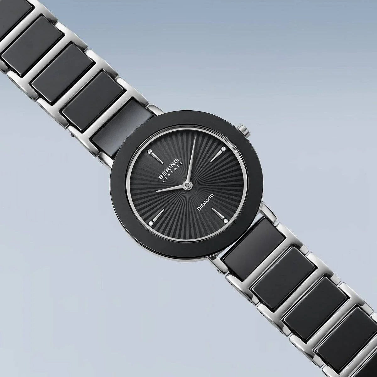 Het Bering dames horloge 11429-702 heeft een moderne zwarte en zilveren band, ronde zwarte wijzerplaat, minimalistische markers, "Diamond" detail op de wijzerplaat en saffierglas - alles tegen een zacht lichtblauw kleurverloop.