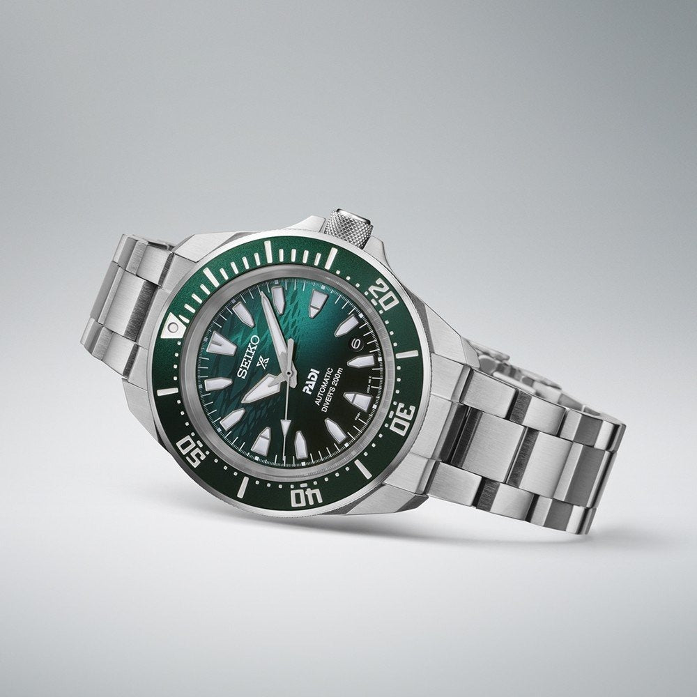 Een Seiko heren horloge SRPL53K1 met een wijzerplaat met groen kleurverloop, bezel, zilveren uurmarkeringen en metalen armband is afgebeeld op een lichtgrijze achtergrond.