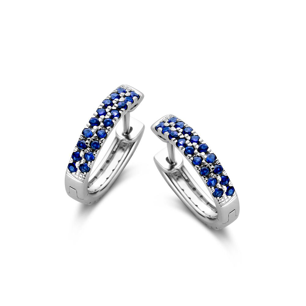 Witgouden oorringen met blauwe saffieren en diamanten, met een moderne, gebogen vorm en een glanzende afwerking.