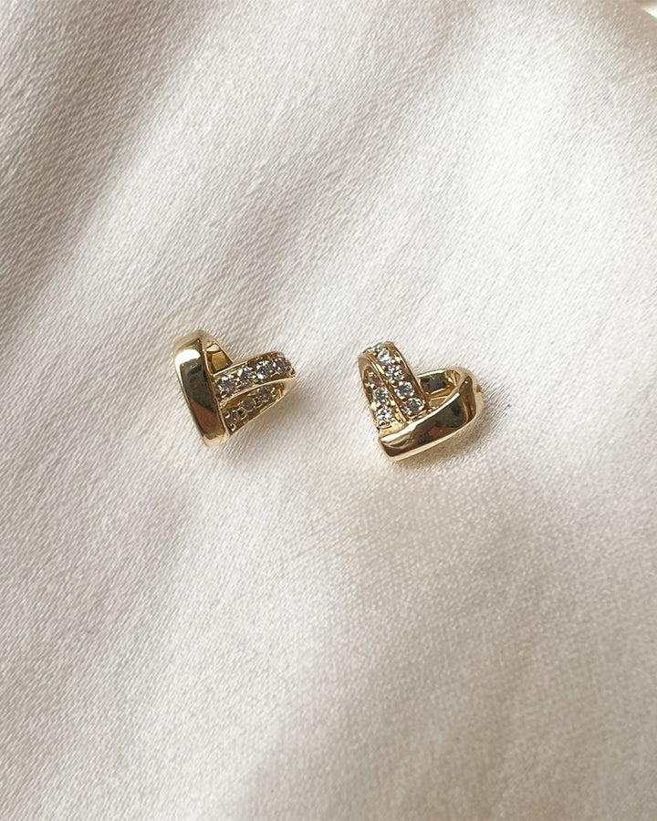 De Geelgouden Oorbellen in Hartvorm met Diamant van Excellent Jewelry zijn elegante 14 karaat oorstekers, schitterend gepresenteerd op een zachte witte satijnen ondergrond.