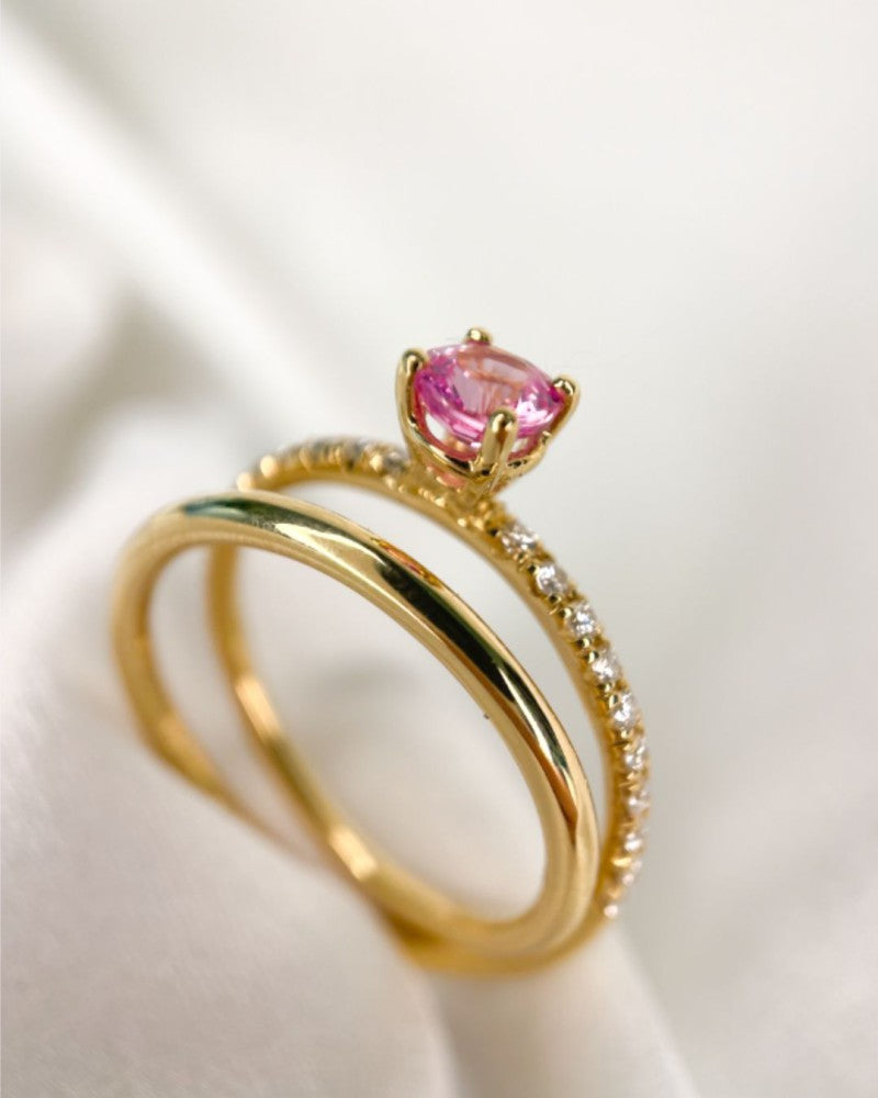 Twee 18kt geelgouden ringen van Excellent Jewelry, uit de Van der Kooij Luxe Sieraad lijn-één met hartvormige roze saffier, de ander met kleine diamanten-zijn stijlvol gestapeld op zachte witte stof.