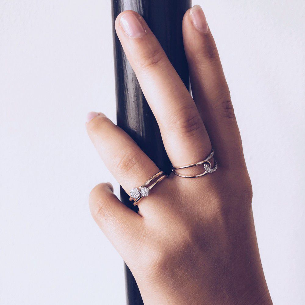 Een hand met een lichte huidskleur houdt een zwarte stok vast en toont de Excellent Jewelry 14-Karaats Bicolor Gouden Damesring met Briljant Geslepen Diamant aan de ringvinger. De achtergrond is effen en lichtgekleurd.