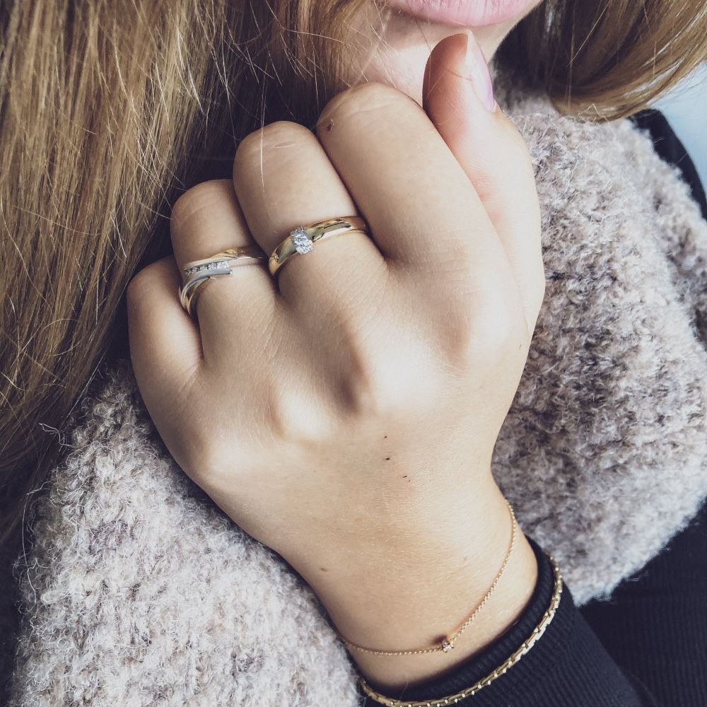 Een close-up van een hand met de 14-karaats bicolor gouden slagring met briljant geslepen diamanten van Excellent Jewelry, samen met andere sieraden en een beige sjaal, straalt tijdloze elegantie uit.