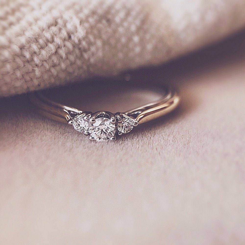 Een close-up van de Excellent Jewelry Bicolor Geel- en Witgouden Ring met Briljant 0.19 crt, elegant vervaardigd uit 14 karaat goud met drie briljanten, getoond op zacht beige stof met een gezellige getextureerde achtergrond.