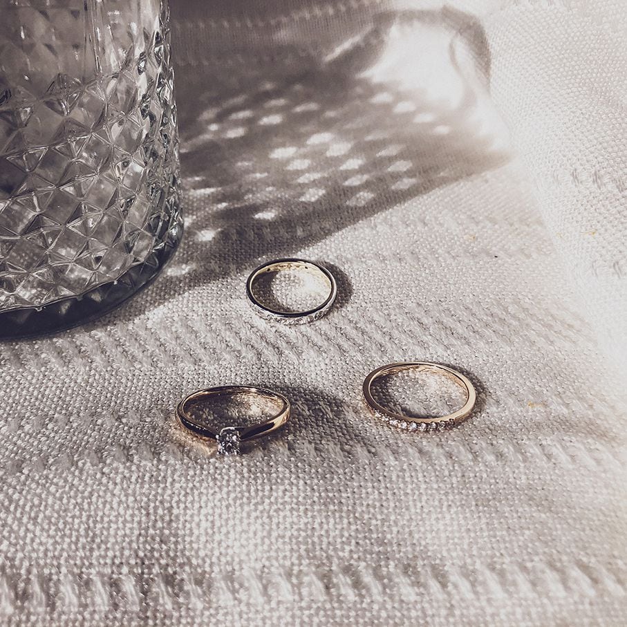 De Elegante Bicolor Gouden Ring met Briljanten 0.19 crt. van Excellent Jewelry rust op witte stof met textuur naast een facet geslepen glas, waarbij het zonlicht zachte schaduwen en patronen werpt.