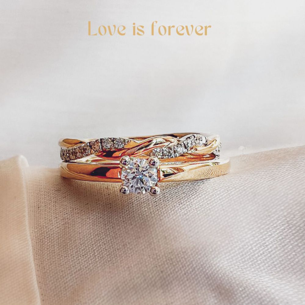 De Bicolor Gouden Ring met Gevlochten Design en Fonkelende Briljanten (0.19 crt.) van Excellent Jewelry roest op een zachte stof. Boven de ring staat de tekst: Liefde is voor altijd.
