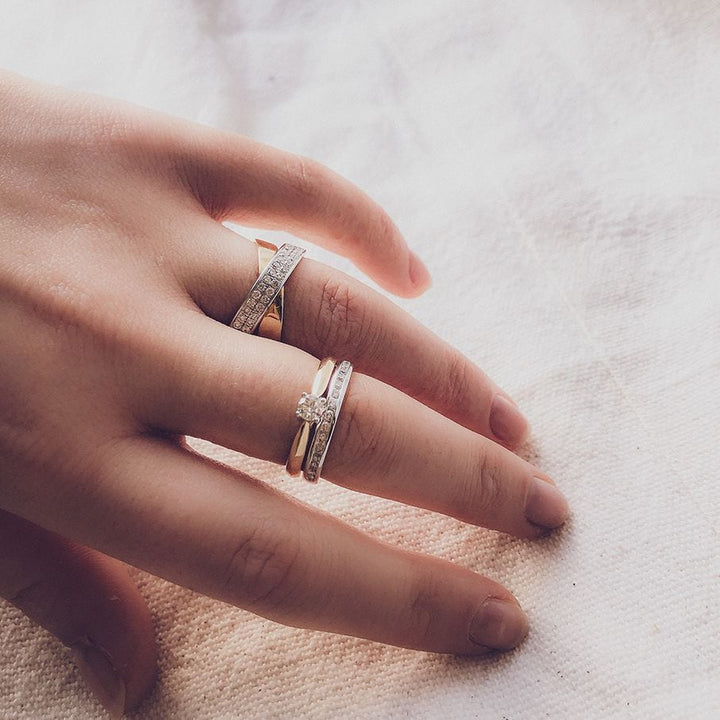 Een close-up van een hand die drie Bicolor Geel- en Witgouden Ringen met Diamant - 0,24 ct van Excellent Jewelry draagt, met briljant geslepen diamant en elegante geelgoud witgouden banden met een delicaat, tijdloos ontwerp.