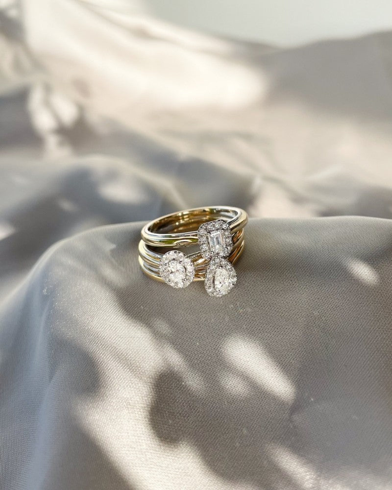 De Excellent Jewelry 14k Bicolor Gold Ring heeft een ovaal diamanten hart in een entourage zetting, elegant weergegeven op zacht, lichtgrijs satijn met zachte patronen van licht en schaduw.