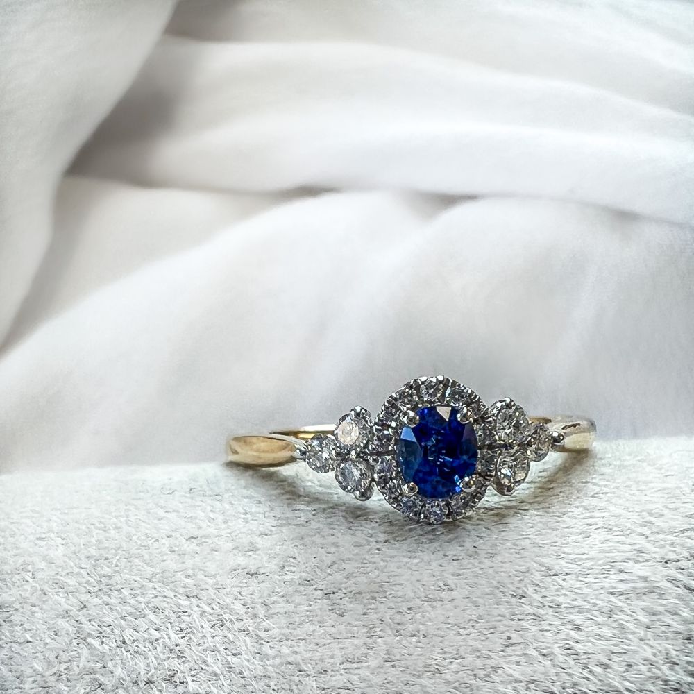 De 14-karaats bicolor gouden damesring met blauwe saffier en vintage diamanten zetting van Excellent Jewelry ligt op een zachte witte stof.