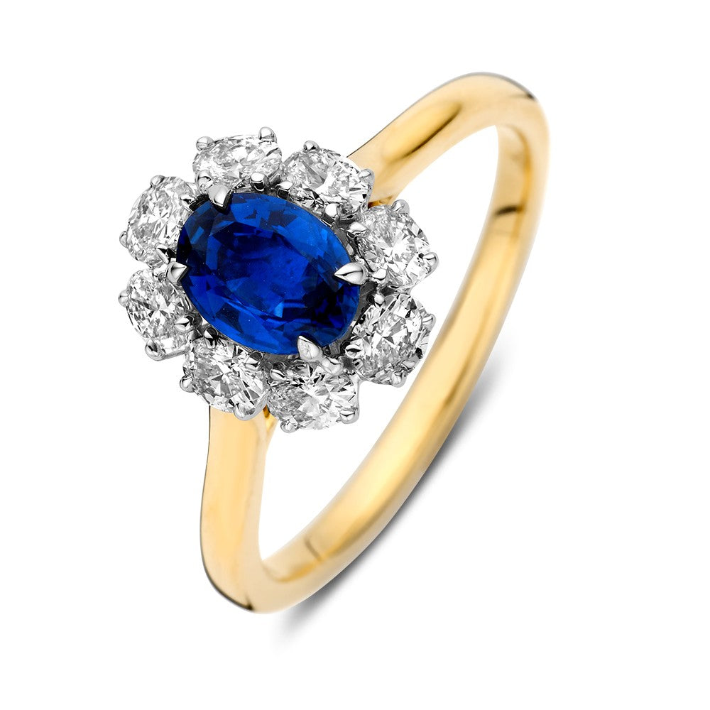 De Ring bicolor briljant + saffier van Excellent Jewelry heeft een ovale blauwe saffier gezet in een bloemenhalo van briljant geslepen diamanten, die tijdloze elegantie weerspiegelt geïnspireerd door de stijl van Lady Di.
