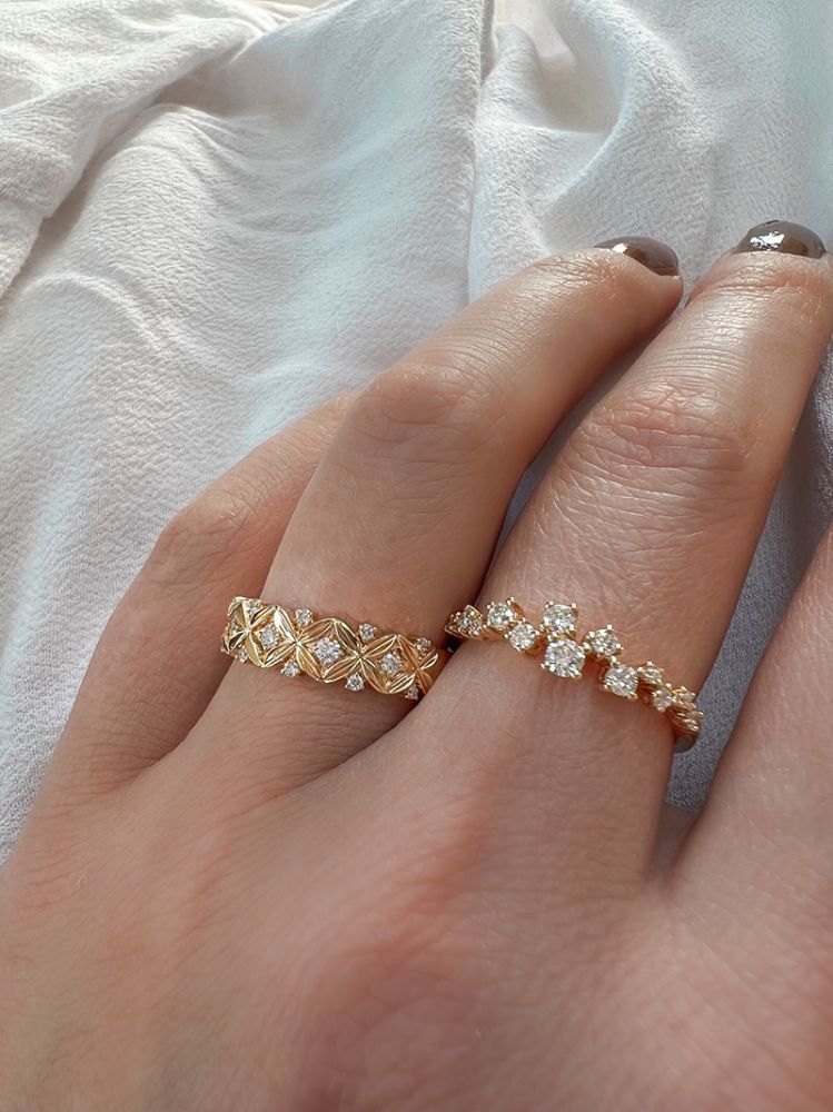Een hand met keurig gemanicuurde nagels draagt de Verfijnde Geelgouden Ring met Diamant - 0,19 crt van Excellent Jewelry, de diamanten zetting glanst zachtjes tegen een lichte stoffen achtergrond.