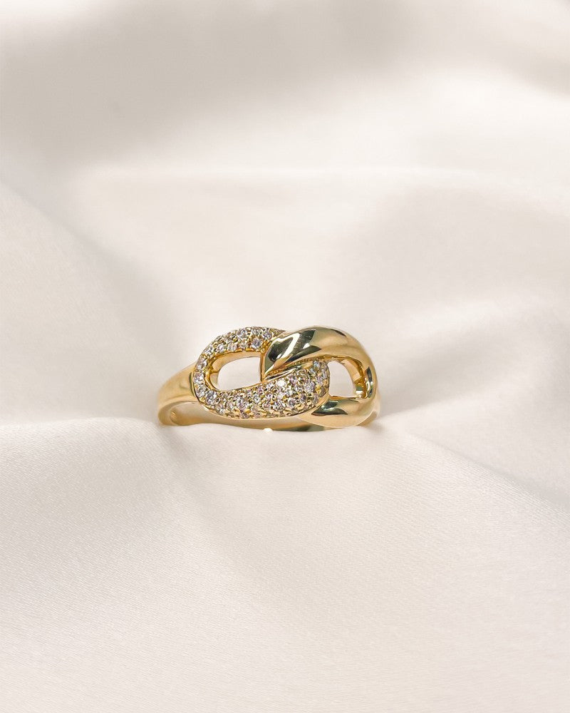 De Geelgouden Ring met Verbonden Schakels en Diamant - 14-Karaat Luxe voor Dames van Excellent Jewelry, deels bezet met briljant geslepen diamant, wordt getoond op een gladde ivoorkleurige stof.