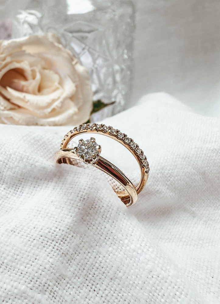 De Verfijnde Geelgouden Ring met Diamanten (0.26 crt., half) van Excellent Jewelry, met centrale diamant en een rij kleinere stenen, ligt op wit textiel - een elegante keuze als verlovingsring.