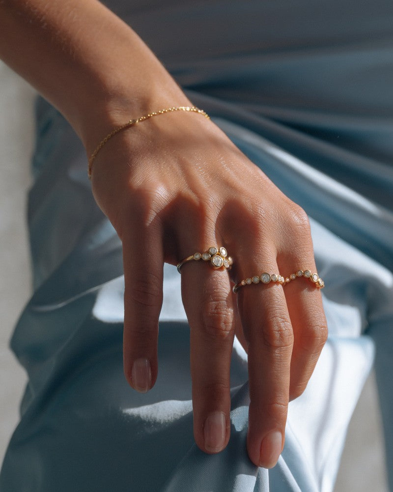 Een hand rust op blauw satijn, draagt de Speelse 14k Geelgouden Ring met 0,37ct diamanten van Excellent Jewelry uit de 'Bubbles' Collectie.