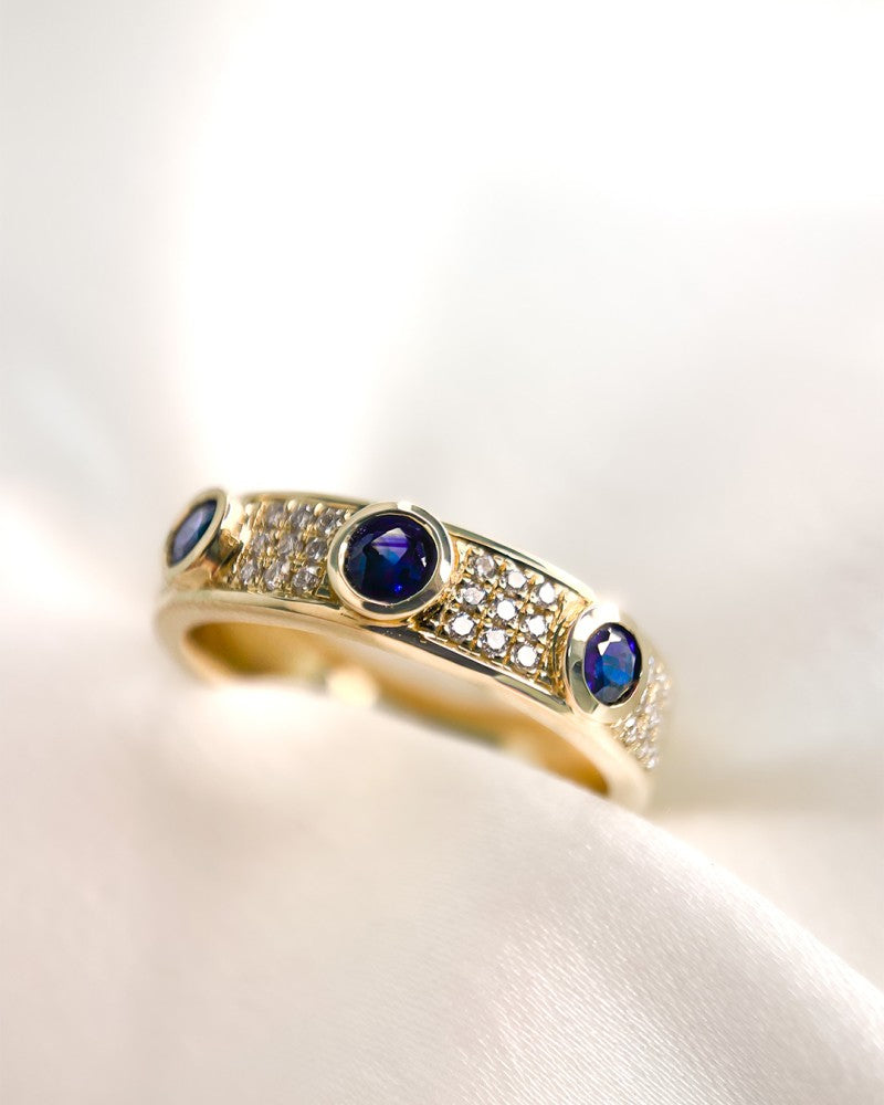 De Excellent Jewelry Geelgouden Ring met Diamant en 3 Blauwe Saffieren (14 karaat, 0.38 crt saffier, 0.17 crt diamant) is afgebeeld op zachte witte stof.