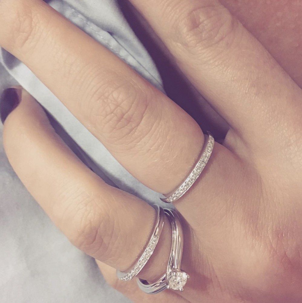 Een close-up van een hand met drie zilveren ringen, waaronder de Excellent Jewelry Witgouden Rijring met Diamanten - Tijdloze Elegantie 0.09 crt., rustend op lichtblauwe stof.