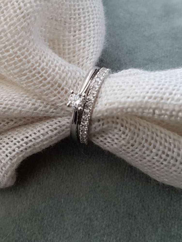De Witgouden Ring met Briljant Diamant - Subtiele Elegantie voor Elke Gelegenheid 0.25 crt. van Excellent Jewelry ligt samen met een bijpassende diamanten band op wit textiel, tegen een zachte grijze achtergrond.