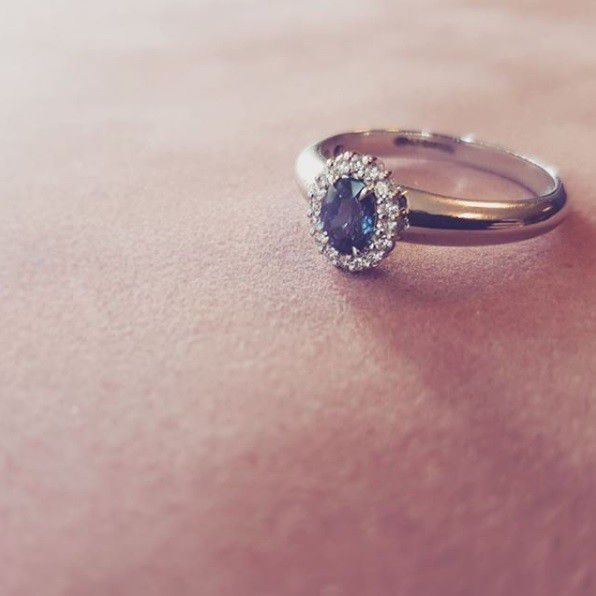 Een close-up van de Witgouden Damesring met Blauwe Saffier en Briljant - Tijdloze Elegantie van Excellent Jewelry, met zijn ovale blauwe saffier en fonkelende diamanten op een zachtroze oppervlak.