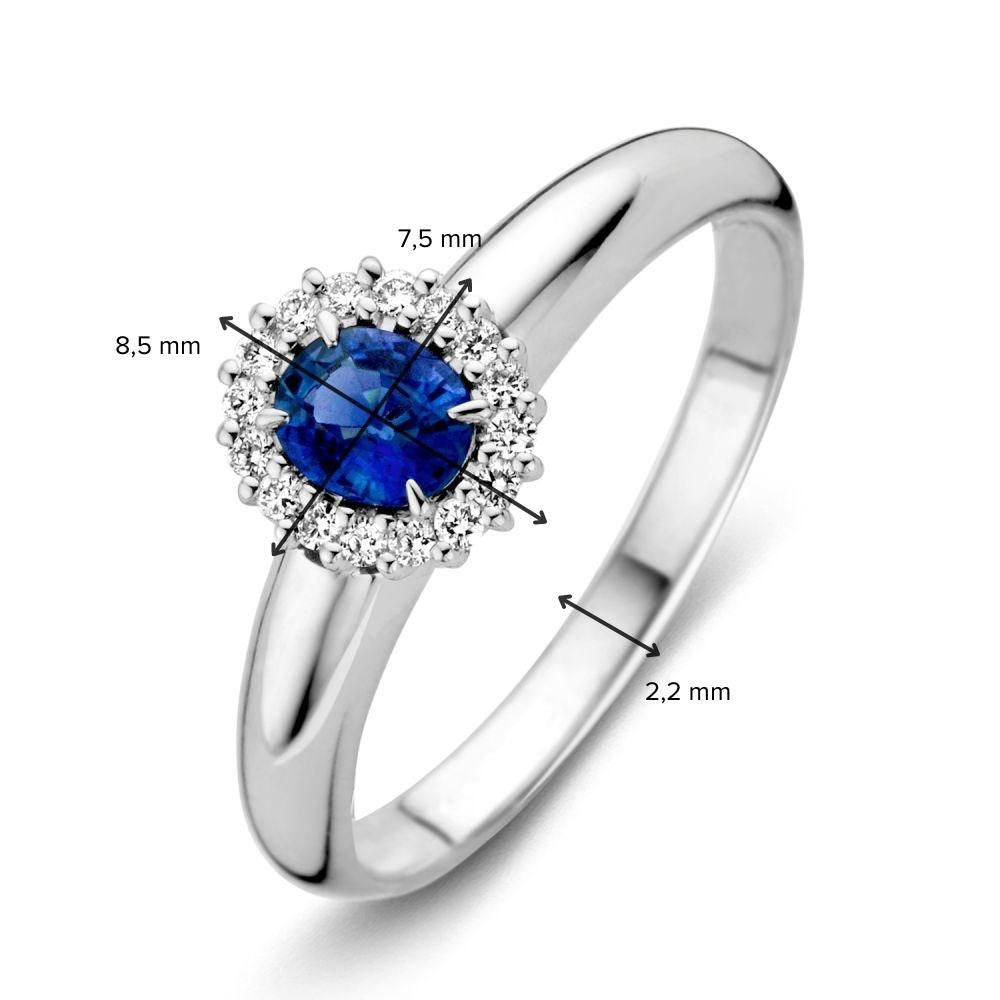 De Witgouden Damesring met Blauwe Saffier en Briljant van Excellent Jewelry heeft een ronde blauwe saffier omringd door diamanten; de zetting meet 8,5 mm x 7,5 mm en de band is 2,2 mm breed.