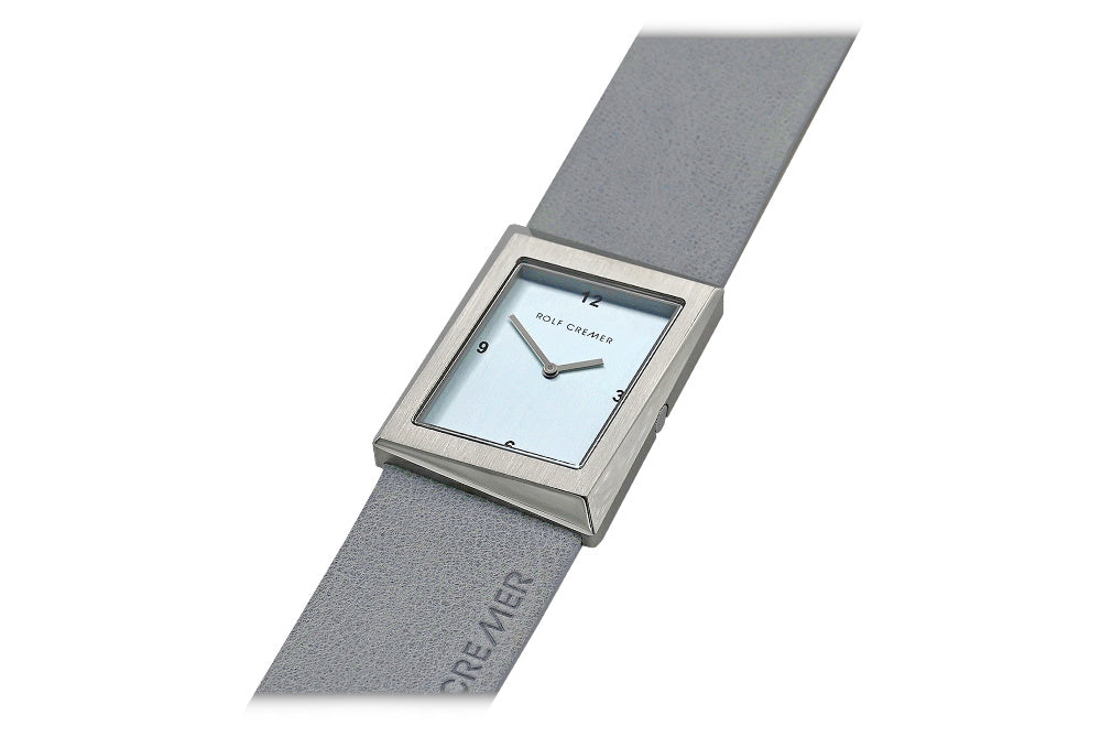 Grijs Rolf Cremer horloge met vierkante kast en lichtblauwe wijzerplaat op een stretchband.