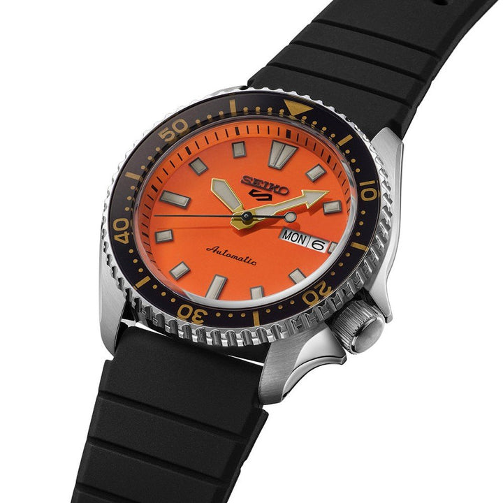 De Seiko 5 Sports heren horloge SRPL89K1 van Seiko heeft een oranje wijzerplaat, zilverkleurige uurmarkeringen, zwarte lunette, zwarte rubberen band en toont de dag en datum op 3 uur.