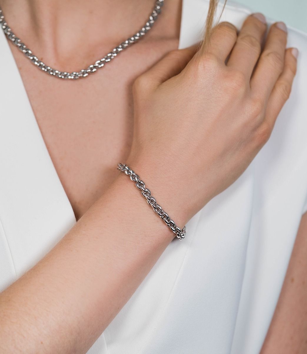Een persoon raakt zijn nek aan, versierd met een Zinzi zilverkleurige ketting en een bijpassende Zia1205 armband, elk 19,5 cm lang. Ze dragen een wit topje, wat de elegante sieraden benadrukt.