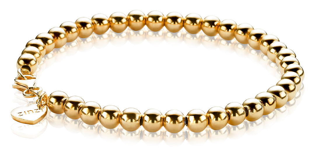 De Zinzi Armband Gold Plated Zia1010 G toont gepolijste elegantie met gouden kralen. Met een hartvormige bedel met Zinzi in de buurt van de sluiting, glanst deze armband schitterend en reflecteert op het oppervlak eronder.