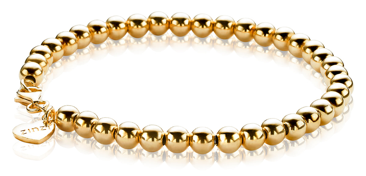 De Zinzi Armband Gold Plated Zia1010 G toont gepolijste elegantie met gouden kralen. Met een hartvormige bedel met Zinzi in de buurt van de sluiting, glanst deze armband schitterend en reflecteert op het oppervlak eronder.